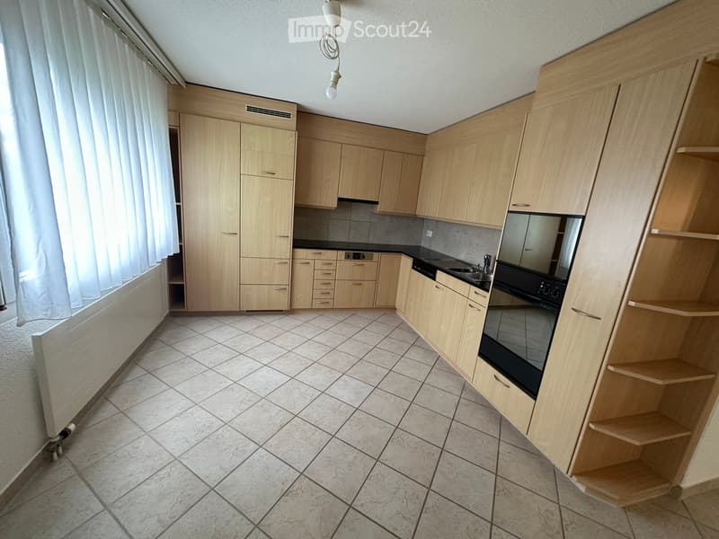 Modern kitchen with light wooden cabinets, tiled floor, and stainless steel appliances including a sink and oven.