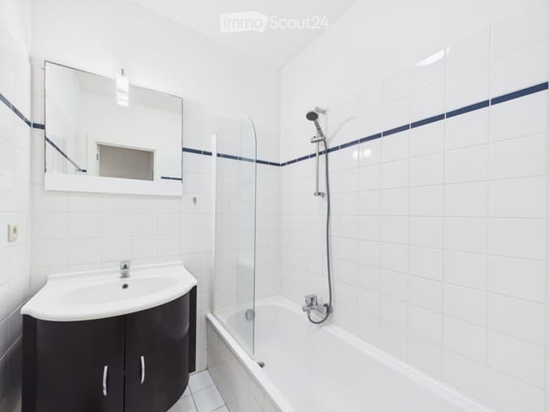 Modern bathroom with white tiles, a dark vanity cabinet, a sink, a mirror, a bathtub, and a glass-enclosed shower area.