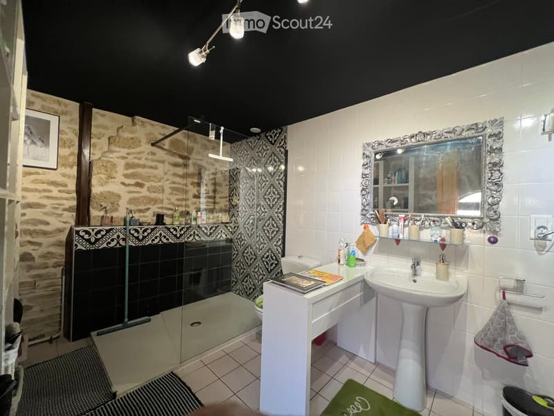 Bathroom with a sink, mirror, toilet, and shower. The walls are tiled, and there is a decorative mirror and a towel visible.