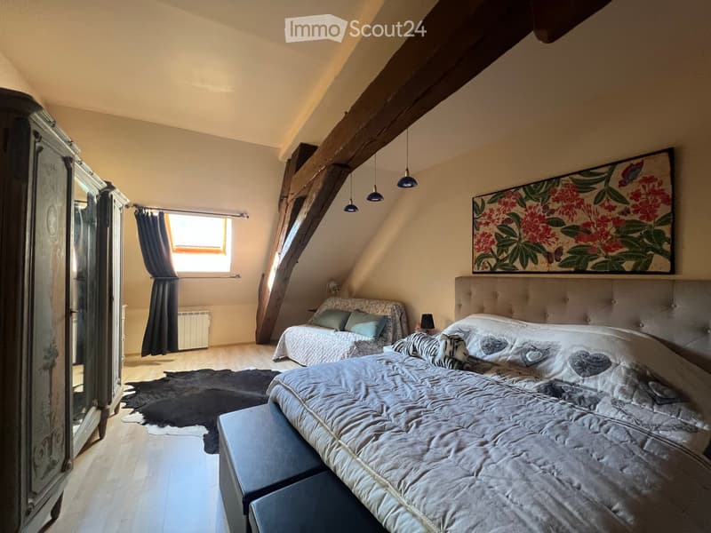 Cozy attic bedroom with wooden beams, two beds, nightstands, a large mirror, and a decorative picture frame on the wall.