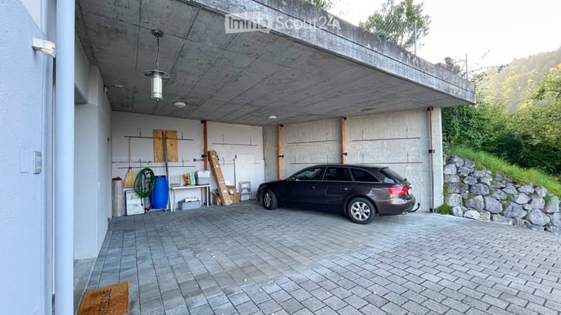 Underground garage with a parked car, storage items, and a concrete ceiling.