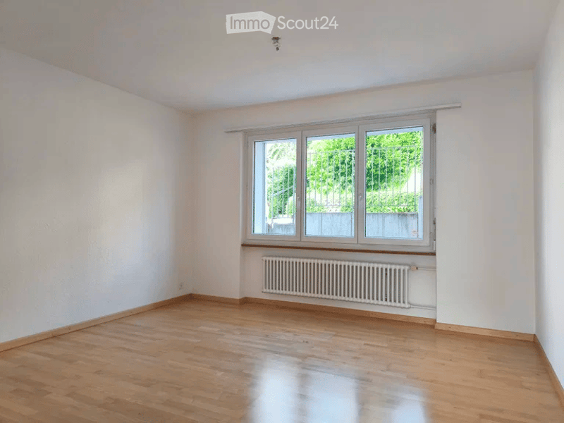 Empty room with wooden flooring, white walls, and a large window with a radiator below it.