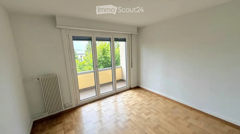 Empty room with wooden flooring, white walls, and large sliding glass doors leading to a balcony.