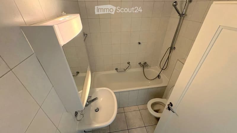 Modern bathroom with a bathtub, toilet, sink, and showerhead. The walls and floor are tiled in light beige tiles.