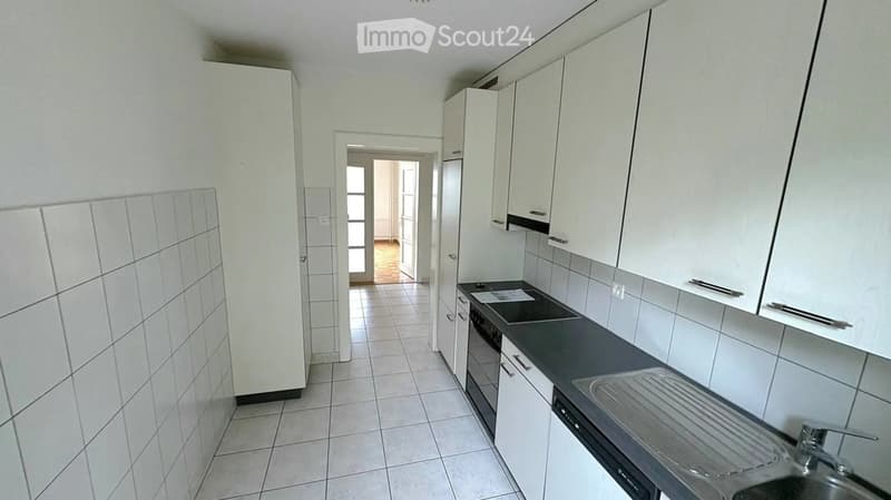 Modern kitchen with white cabinets, tiled walls, and a black countertop. Features a sink, faucet, and oven.