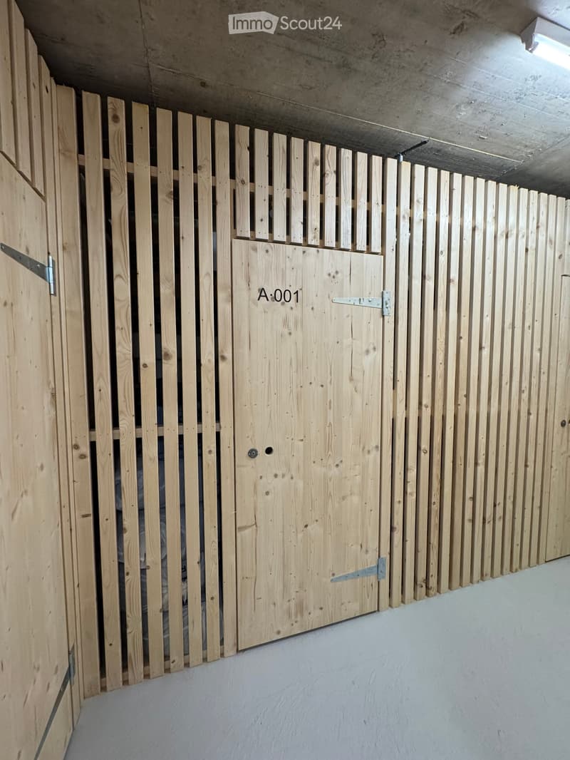 A concrete-floored corridor with a wooden slatted gate and a numbered door labeled 'A:001'.