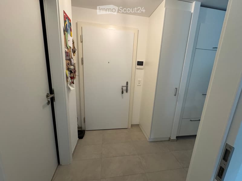 Empty hallway with tiled floor, white walls, and several doors including a closet and a main entrance door.
