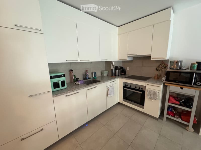 Modern kitchen with white cabinets, granite countertops, and stainless steel appliances including an oven, microwave, and toaster. A small wooden stool is placed near the counter.
