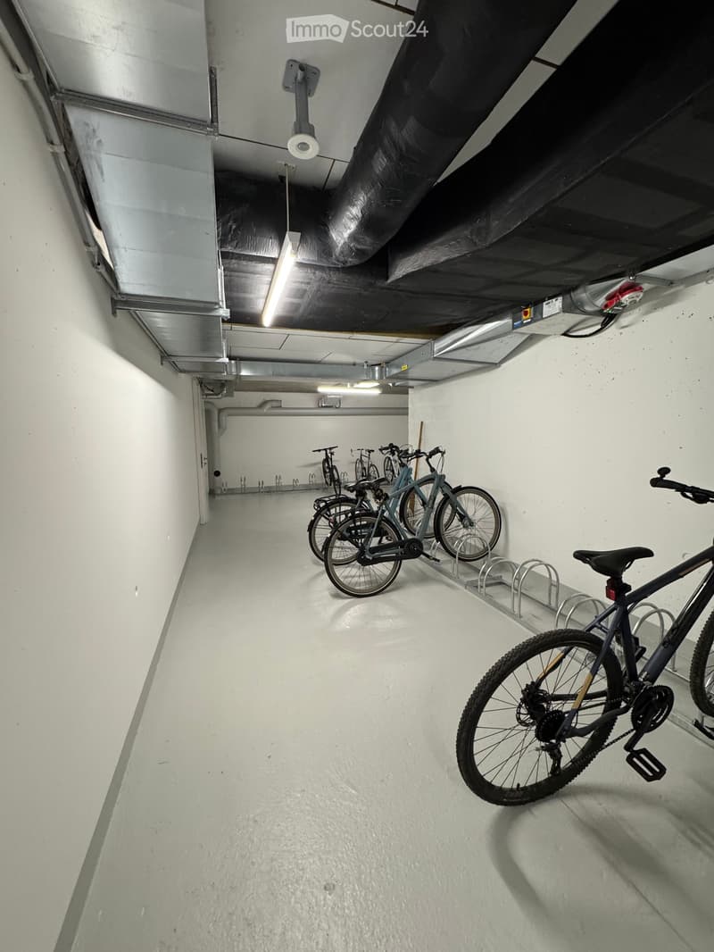 Underground parking area with several bicycles parked on racks, white walls, and industrial lighting.