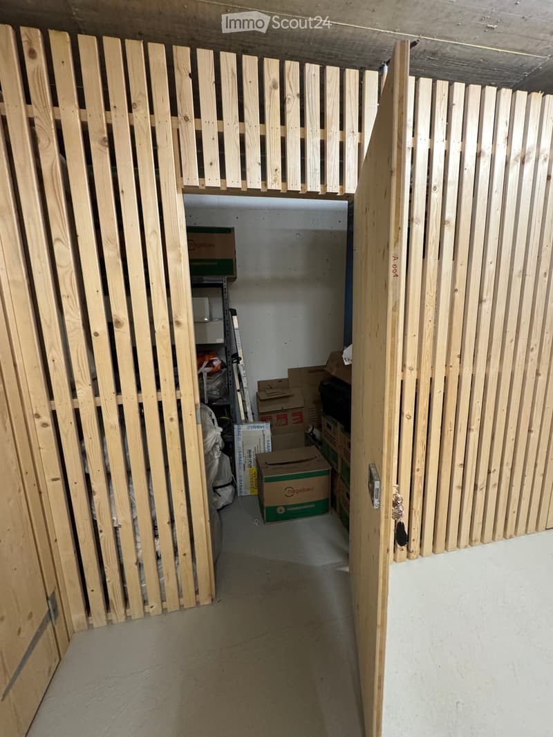 Empty storage area with concrete floor, wooden plank walls, and scattered boxes and items.