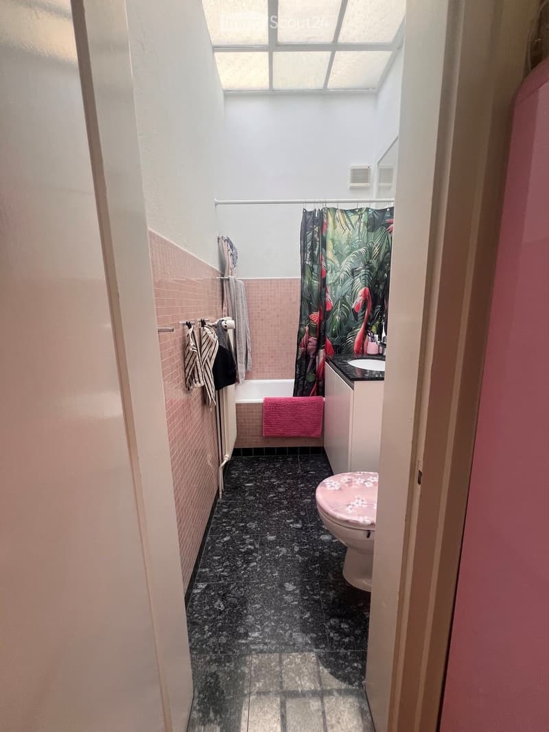Bathroom with pink tiles, dark granite floor, toilet, sink, bathtub, and a colorful shower curtain with flamingo design.