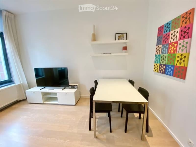 A modern, minimalist room with a white table and chairs, a TV on a white stand, shelves with decorative items, and a colorful abstract painting on the wall.