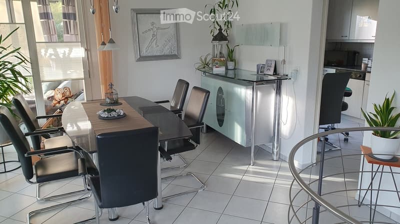 Modern dining area with a wooden table, black chairs, a glass cabinet, and a small round stool with a potted plant.