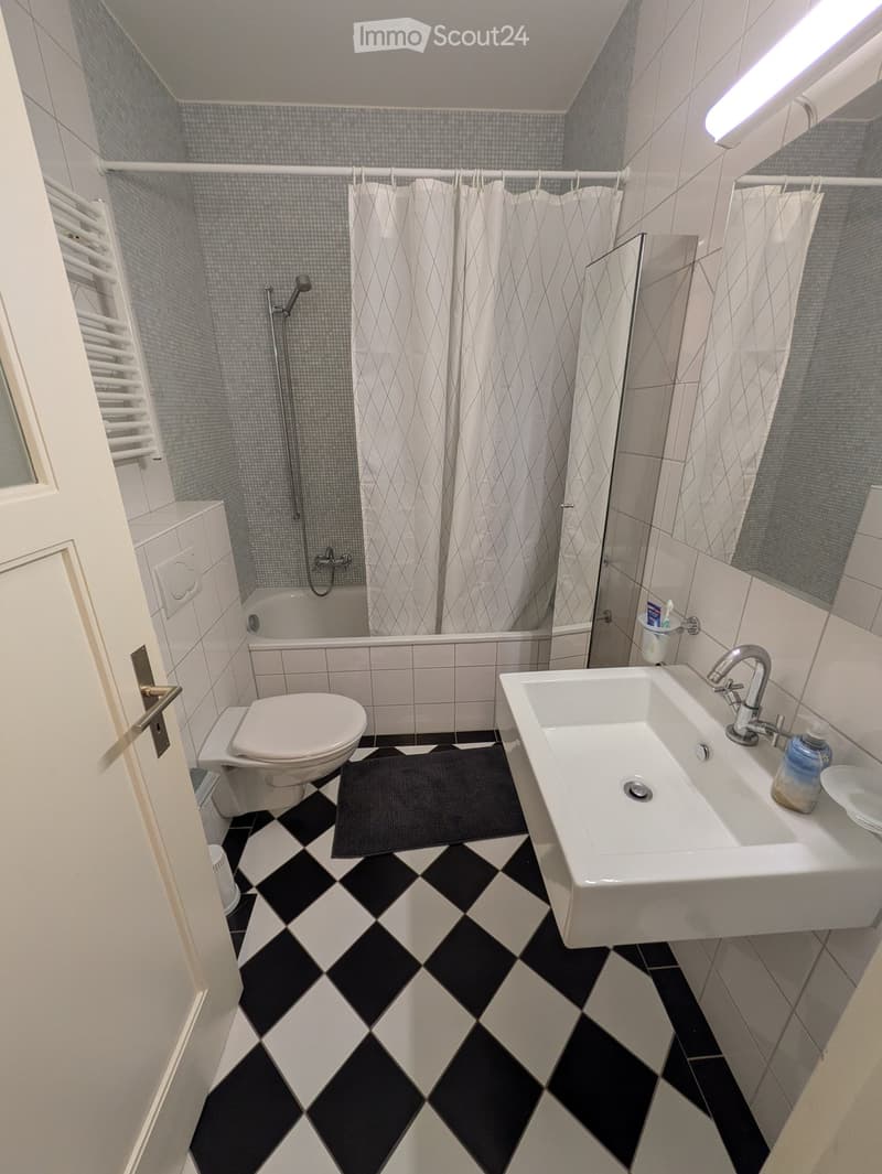Modern bathroom with black and white checkered floor, white sink, toilet, bathtub with shower curtain, and a mirror above the sink.