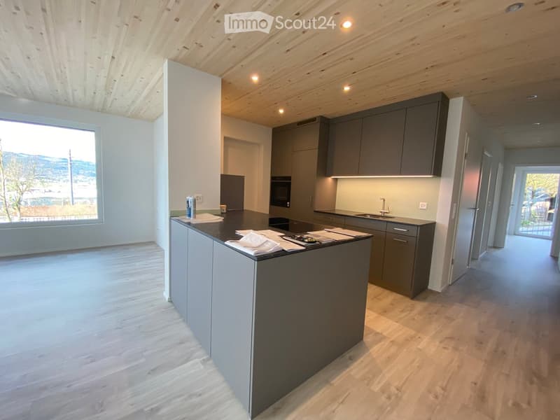 Modern kitchen with grey cabinets, a central island, and a large window overlooking a scenic view.