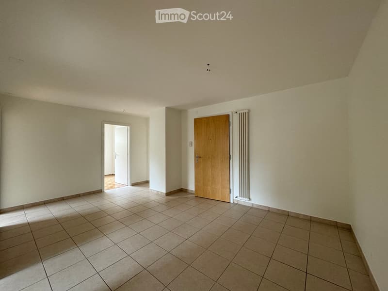 Empty room with tiled floor, beige walls, and two doors, one leading to another room.