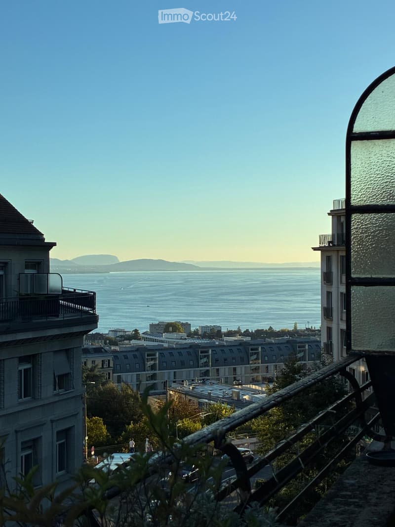 Balcony overlooking a cityscape with a body of water and distant mountains in the background.
