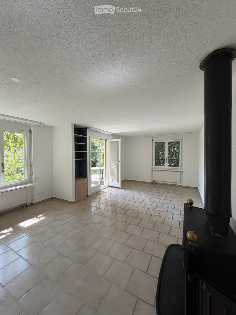 Empty room with tiled floor, white walls, large windows, and a black wood-burning stove. No furniture or personal items are present.