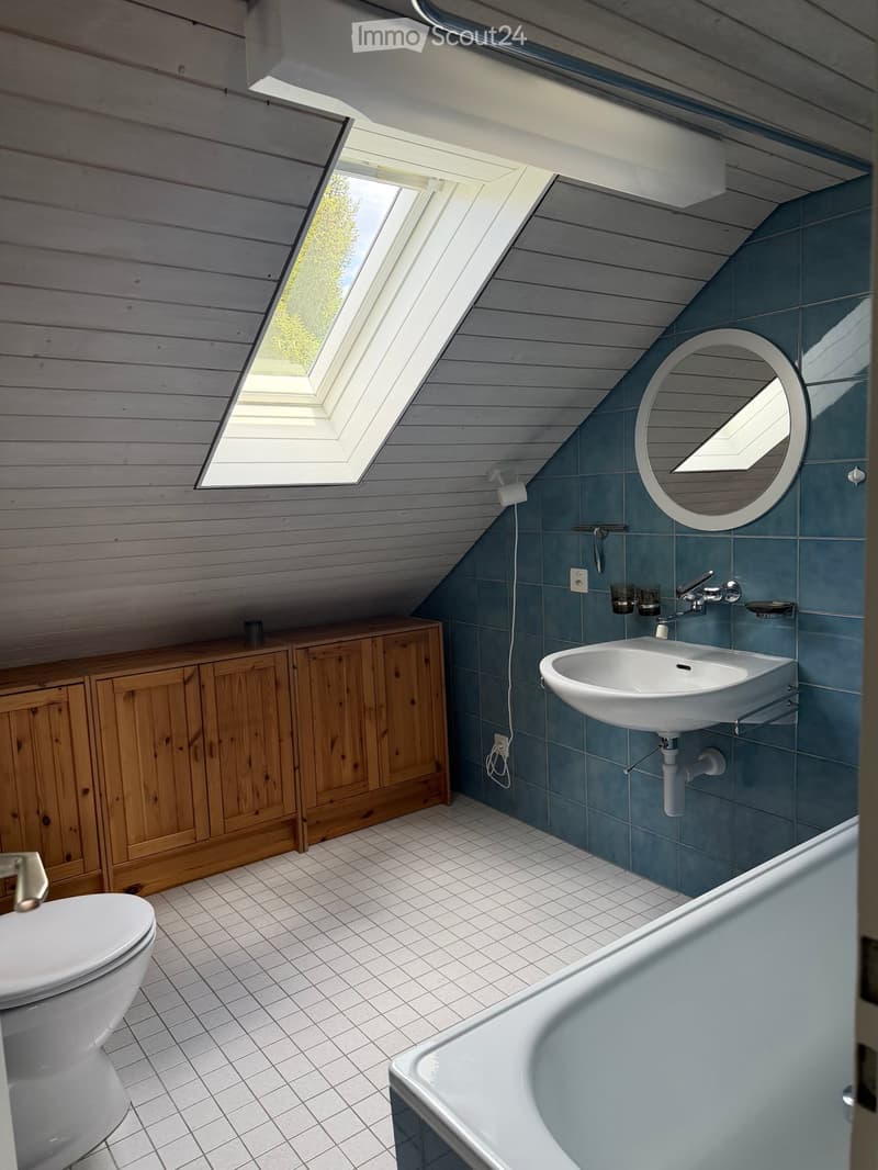 Modern attic bathroom with wooden panel walls, white tiled floor, bathtub, toilet, sink, and wooden cabinet.