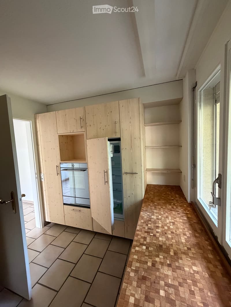 The kitchen features light wooden cabinets, a tiled floor, and a wooden countertop. A refrigerator is visible within the cabinets.