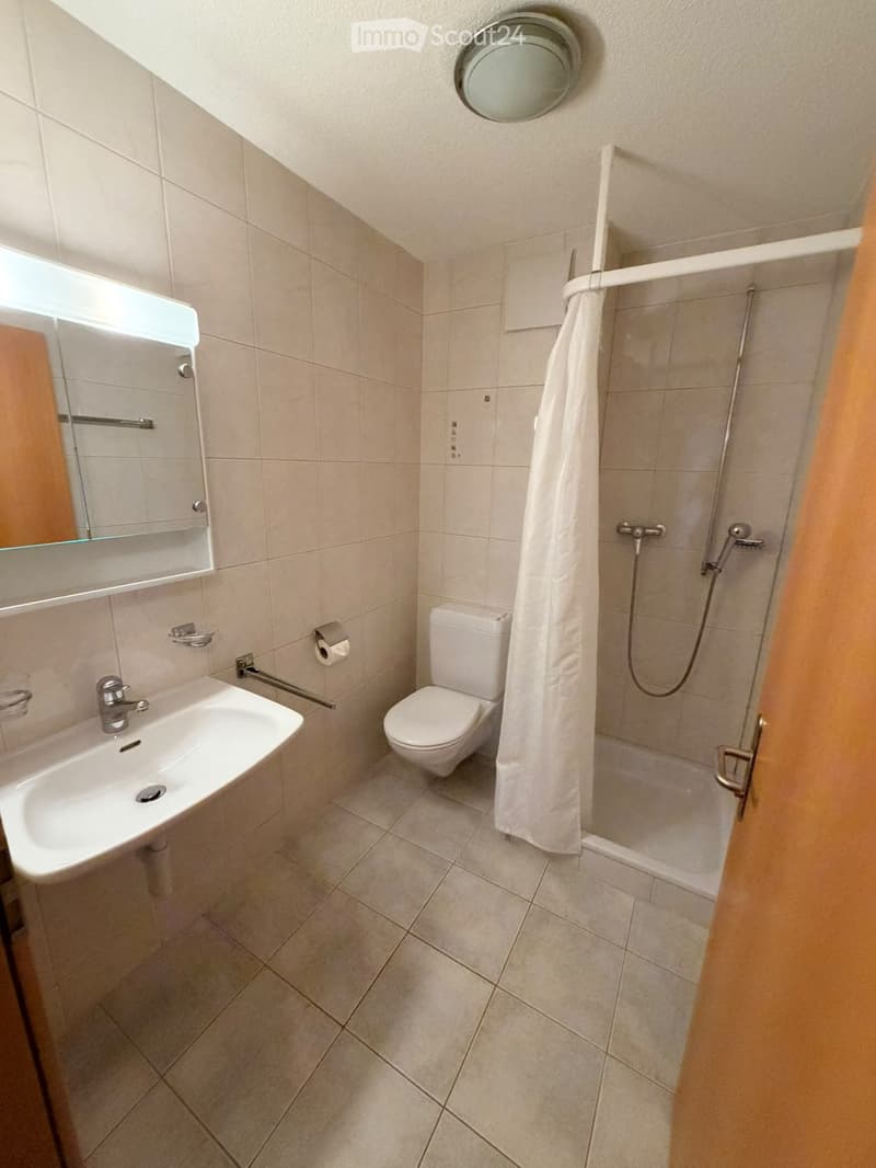 Modern bathroom with beige tiles, a white sink, toilet, shower with a curtain, and a round ceiling light.