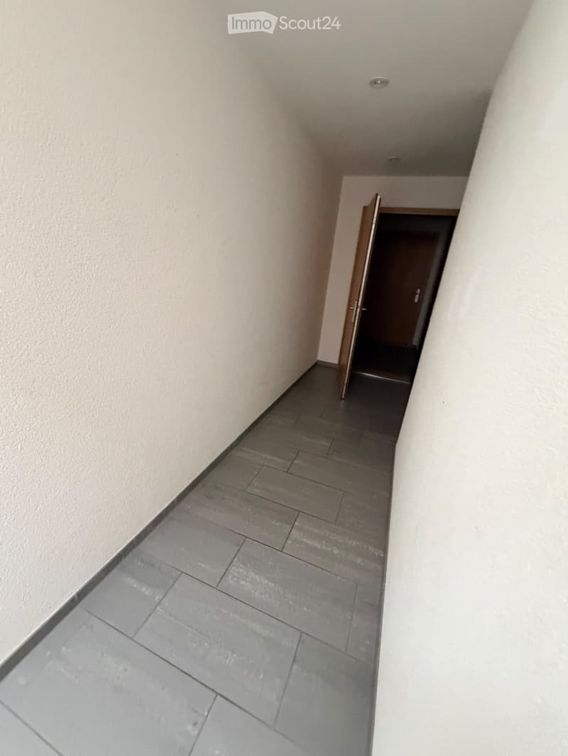 Empty hallway with grey tiled floor and white walls, featuring an open wooden door leading to another room.