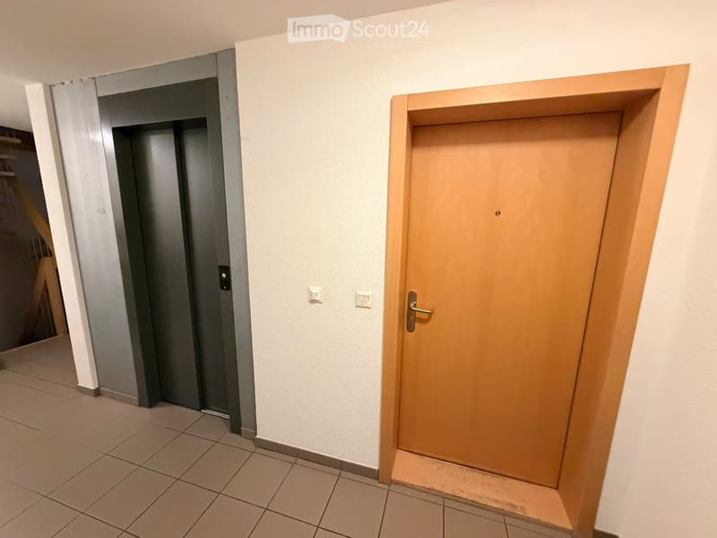 A hallway with tiled flooring, white walls, and two doors: a wooden door and a grey elevator door.