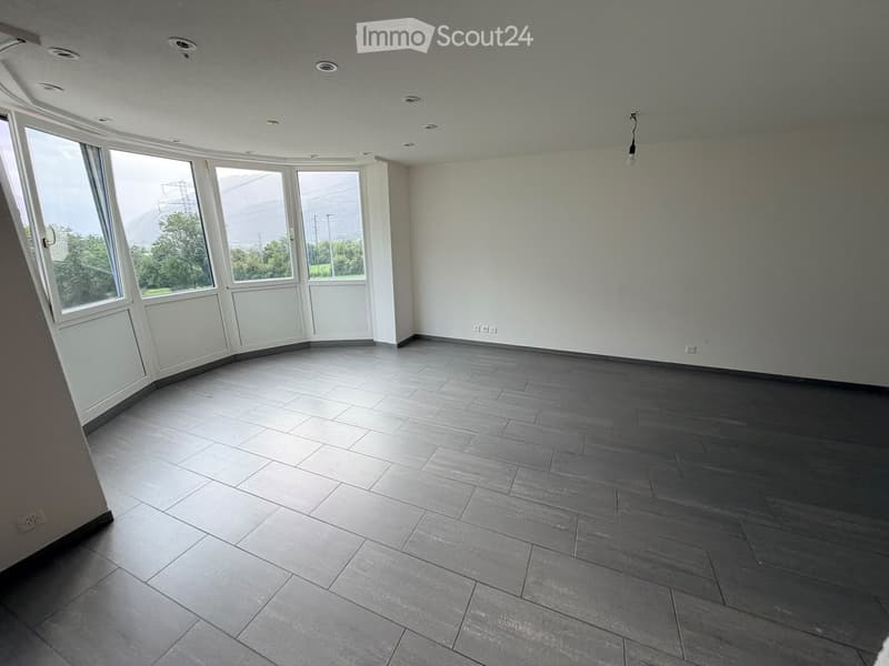 Empty room with grey tiled floor, white walls, large windows, and recessed ceiling lights.
