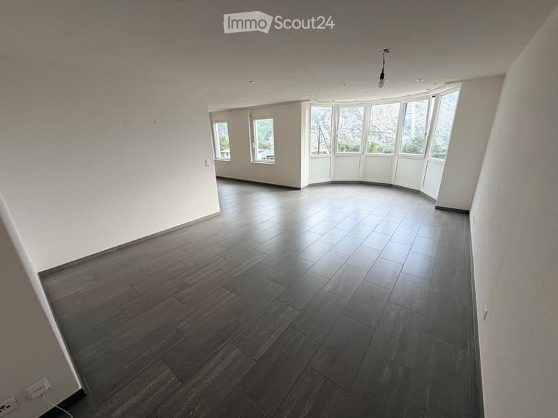 Empty room with wooden flooring, white walls, and large windows offering a scenic view.