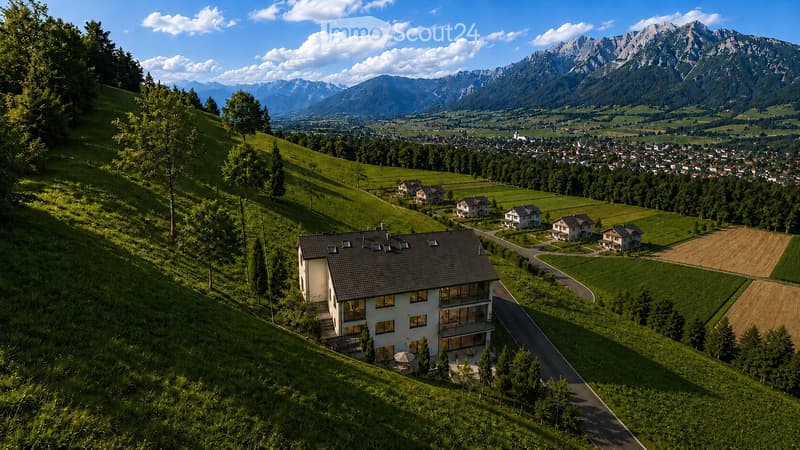 Modern two-story house with large windows and a balcony, situated on a hillside with a scenic mountain view and surrounding greenery.