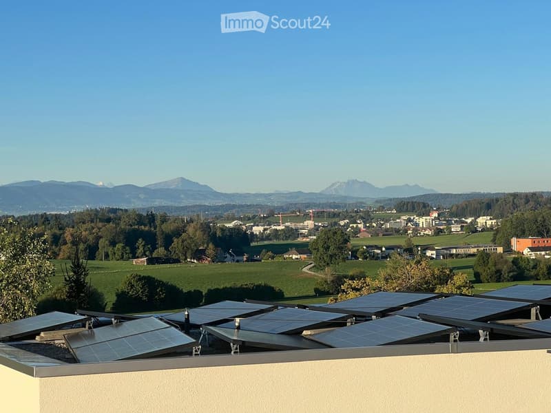 Roof terrace with solar panels, overlooking a rural landscape with fields, trees, and distant mountains.