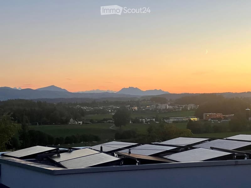 Roof terrace with solar panels, overlooking a town and distant mountains at sunset.