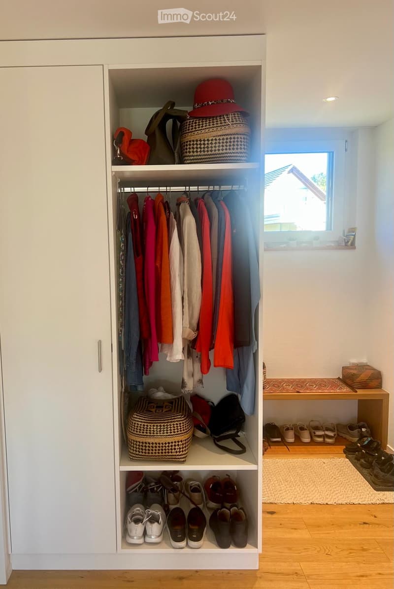Well-organized hallway closet with multiple sections for hanging clothes, storing shoes, and keeping accessories. The closet features white cabinetry, multiple shelves, and a variety of neatly arranged items including shoes, bags, and hats.