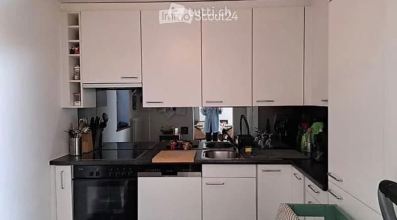 Modern kitchen with white cabinets, black countertops, stainless steel sink, and various kitchen utensils.