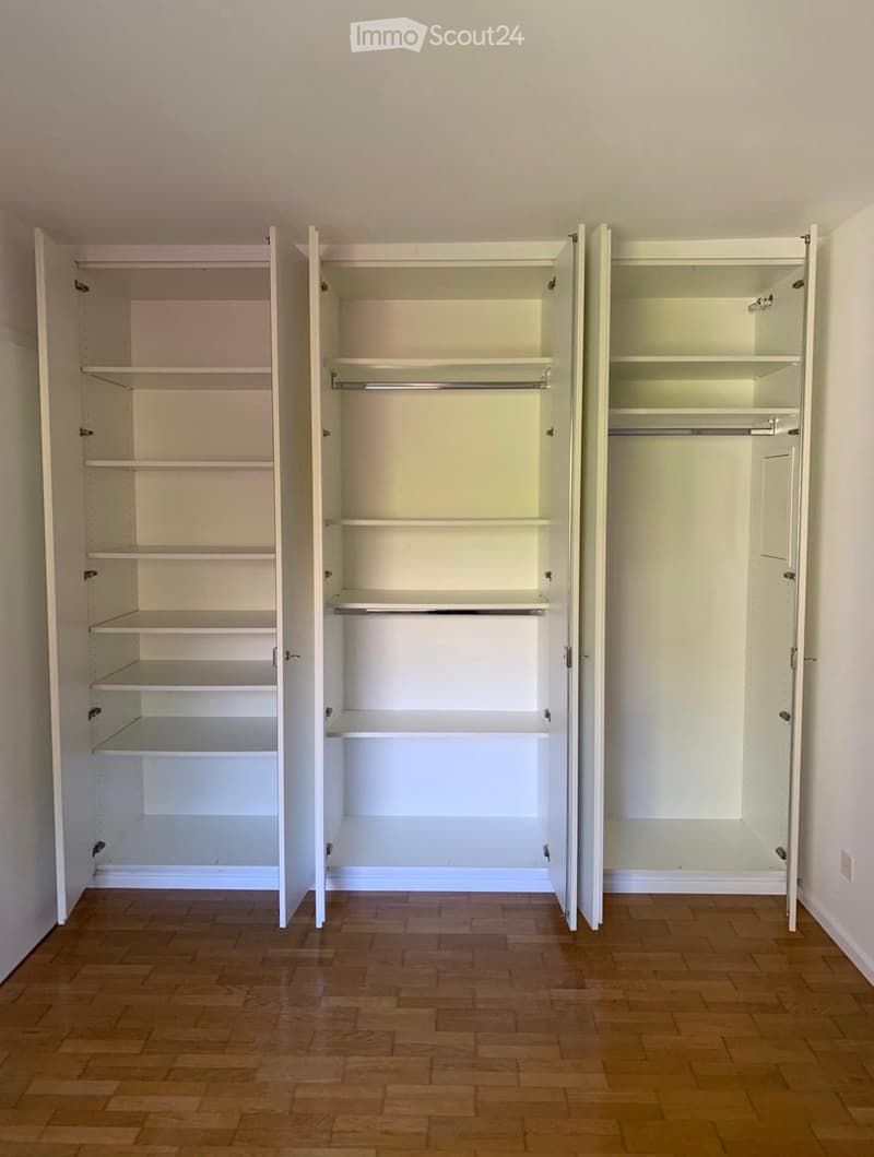Empty room with wooden flooring and three large, open white built-in wardrobes with multiple shelves and hanging rods.