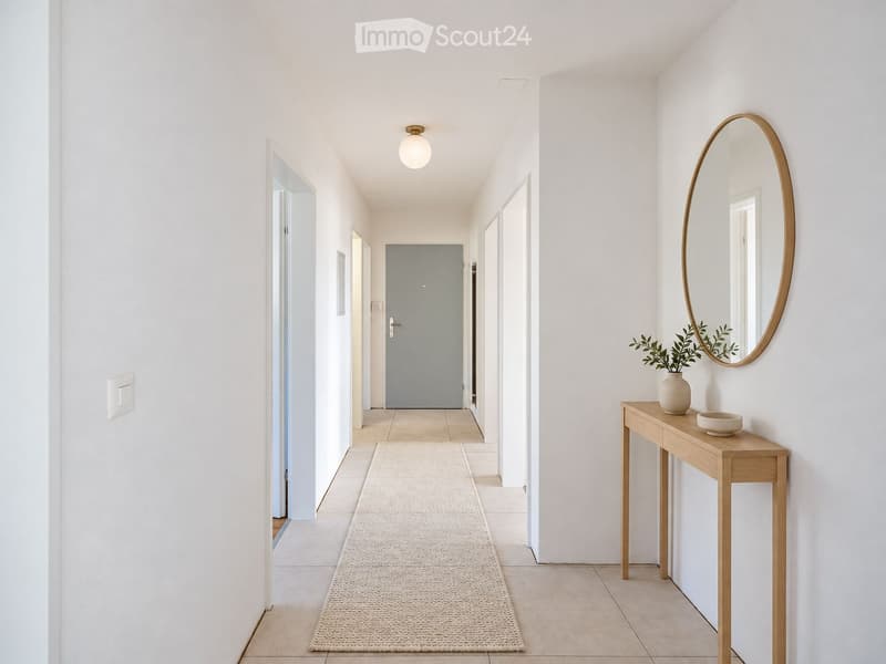 A clean, modern hallway with white walls, a light-colored tiled floor, and a round mirror on the wall. A small wooden console table with a vase and bowl sits to the right, and a light fixture hangs from the ceiling.