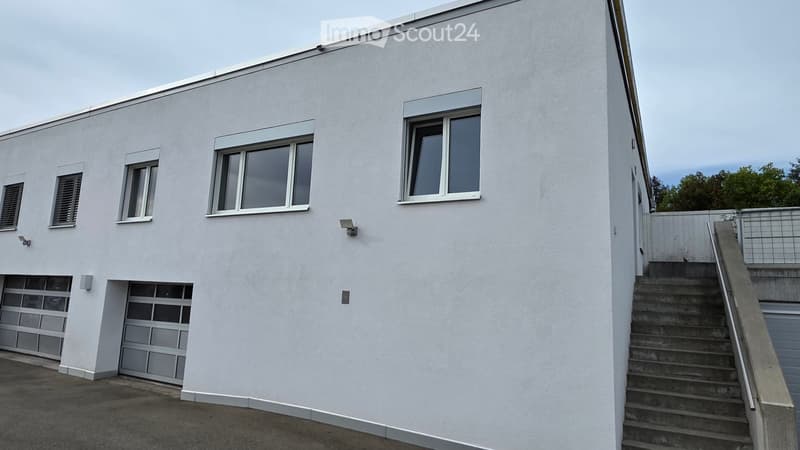 Modern two-story building with white exterior, large garage doors, multiple windows, and a staircase leading to an upper level.