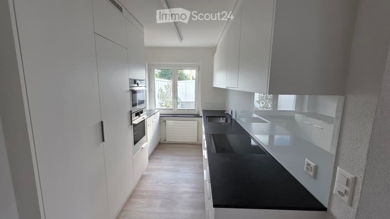 Modern kitchen with white cabinets, black countertops, and a central island. Features include a sink, faucet, built-in oven, and radiator.