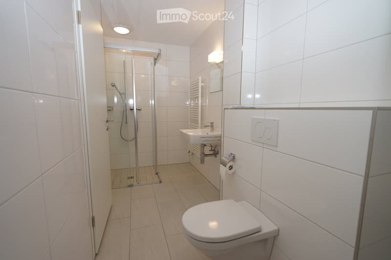 Modern bathroom with white tiles, a toilet, a sink, a shower, and a mirror.