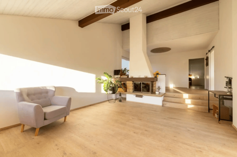 Bright living room with wooden flooring, large window, fireplace, sofa, small table, and plant.