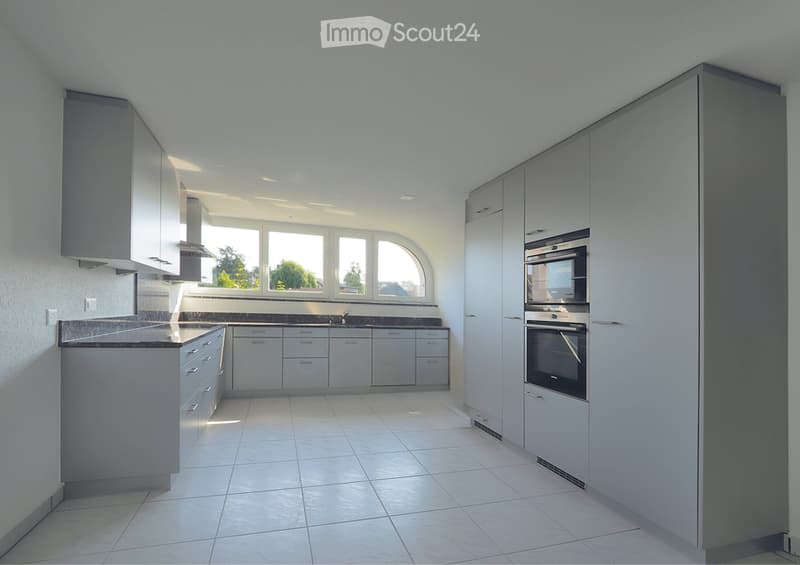 Modern kitchen with grey cabinets, white tiled floor, and large windows. Features a sink, oven, and ample storage space.