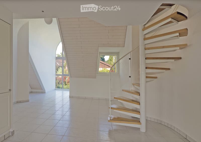 Modern hallway with a spiral staircase featuring wooden steps and white railings, large windows allowing natural light, and a clean, minimalist design with white walls and tiled flooring.