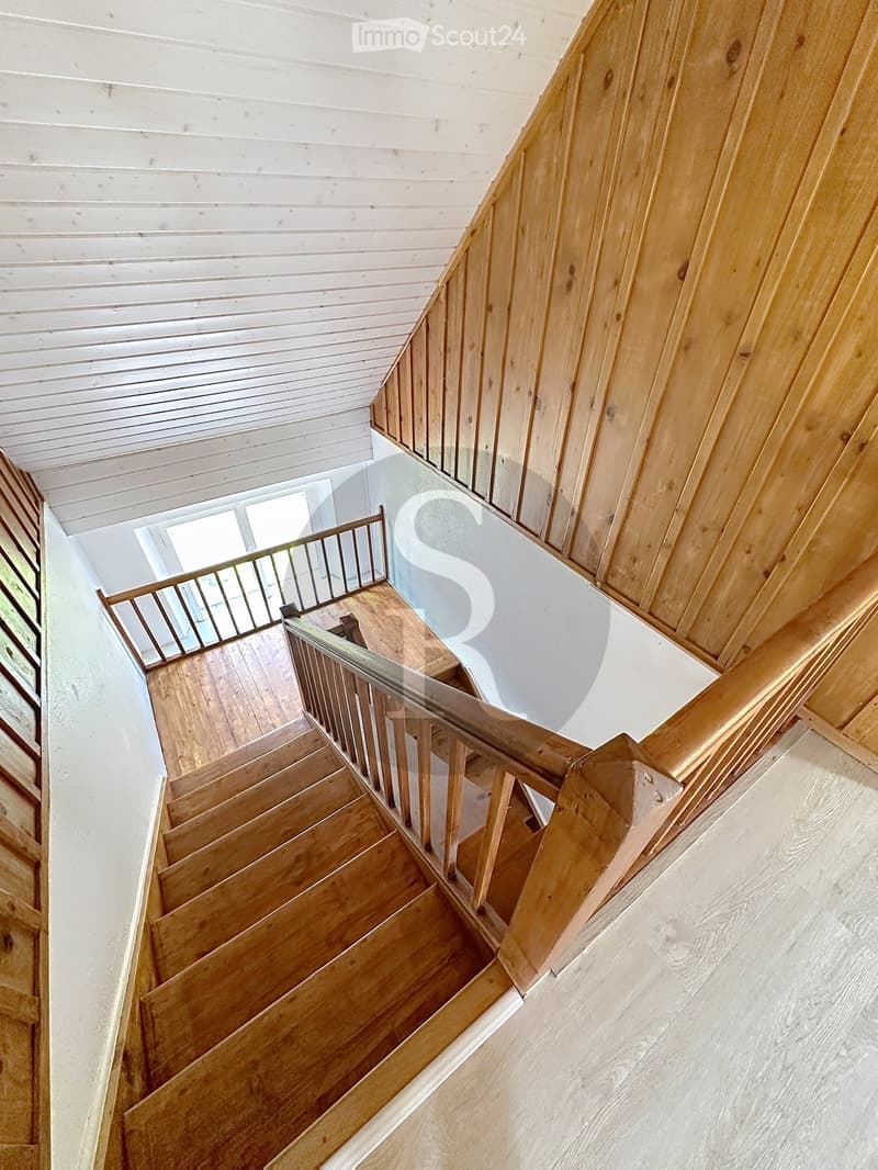 Wooden staircase with a glass railing, white paneled ceiling, and light-colored walls.
