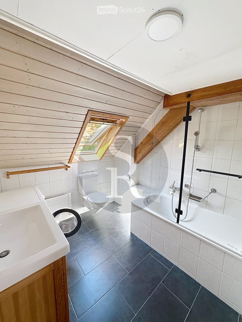 Modern bathroom with white tiles, a toilet, a bathtub with a shower, a sink, and a skylight window providing natural light.