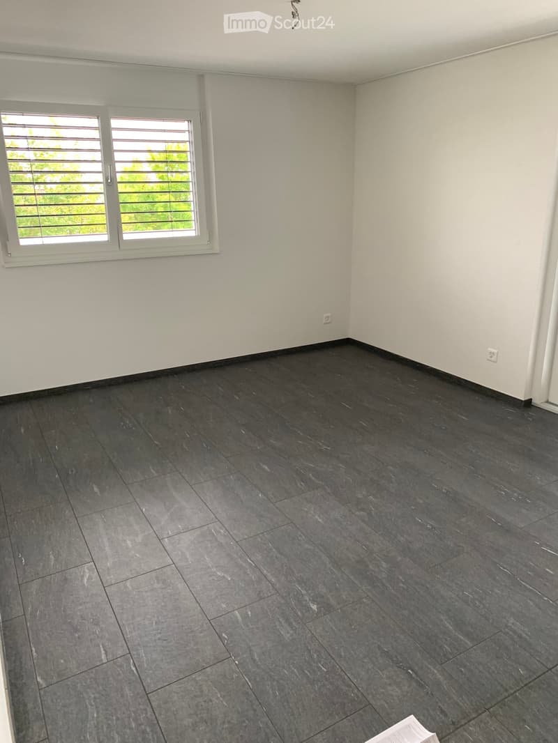 Empty room with dark grey tiled flooring and white walls, featuring a large window with blinds and white frame.