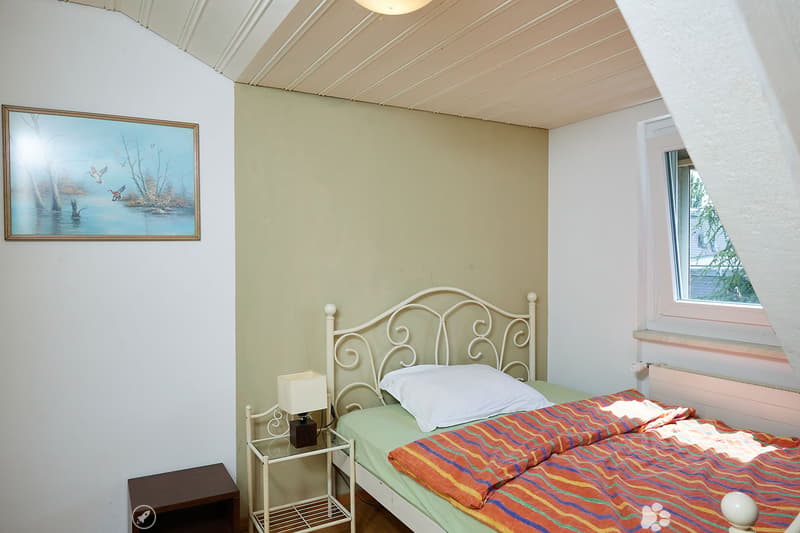 Cozy bedroom with a single bed, white metal headboard, colorful striped bedspread, nightstand with lamp, and a framed picture on the wall.