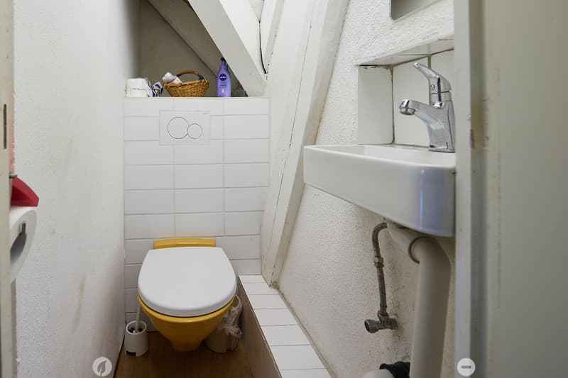 Compact bathroom with white tiled walls, a white toilet with a yellow seat, a white sink with a chrome faucet, and a small wicker basket on the shelf above the toilet.
