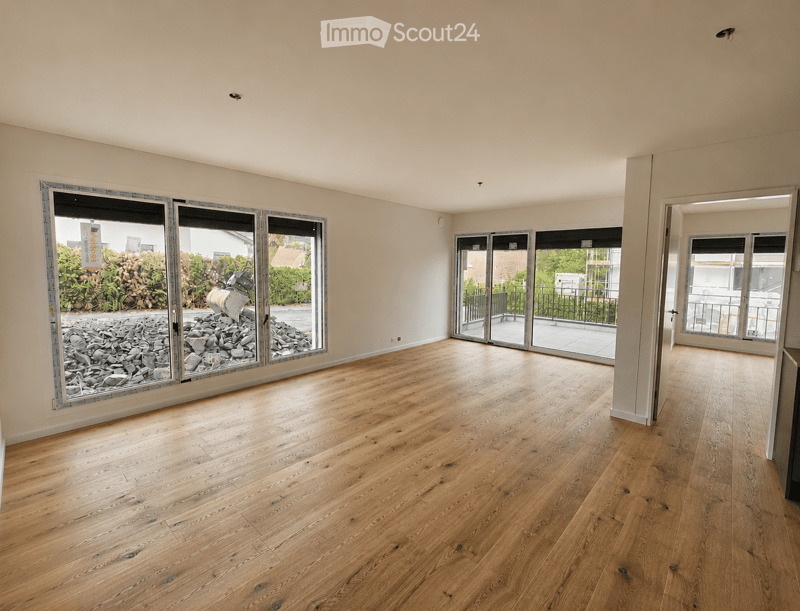 Empty room with wooden flooring, large windows, and sliding doors leading to a balcony area.