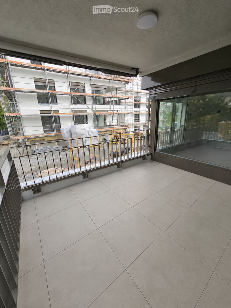 Empty balcony with tiled floor, metal railing, and large glass sliding door leading to the interior.