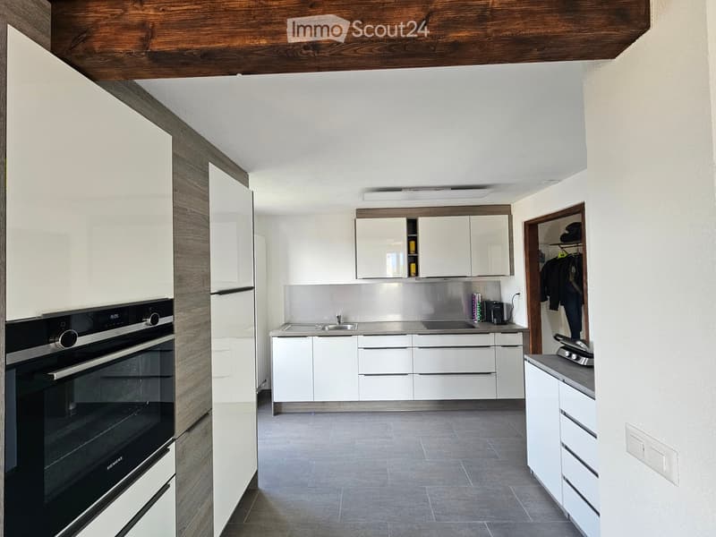 Modern kitchen with white cabinets, stainless steel appliances, and a wooden ceiling beam.